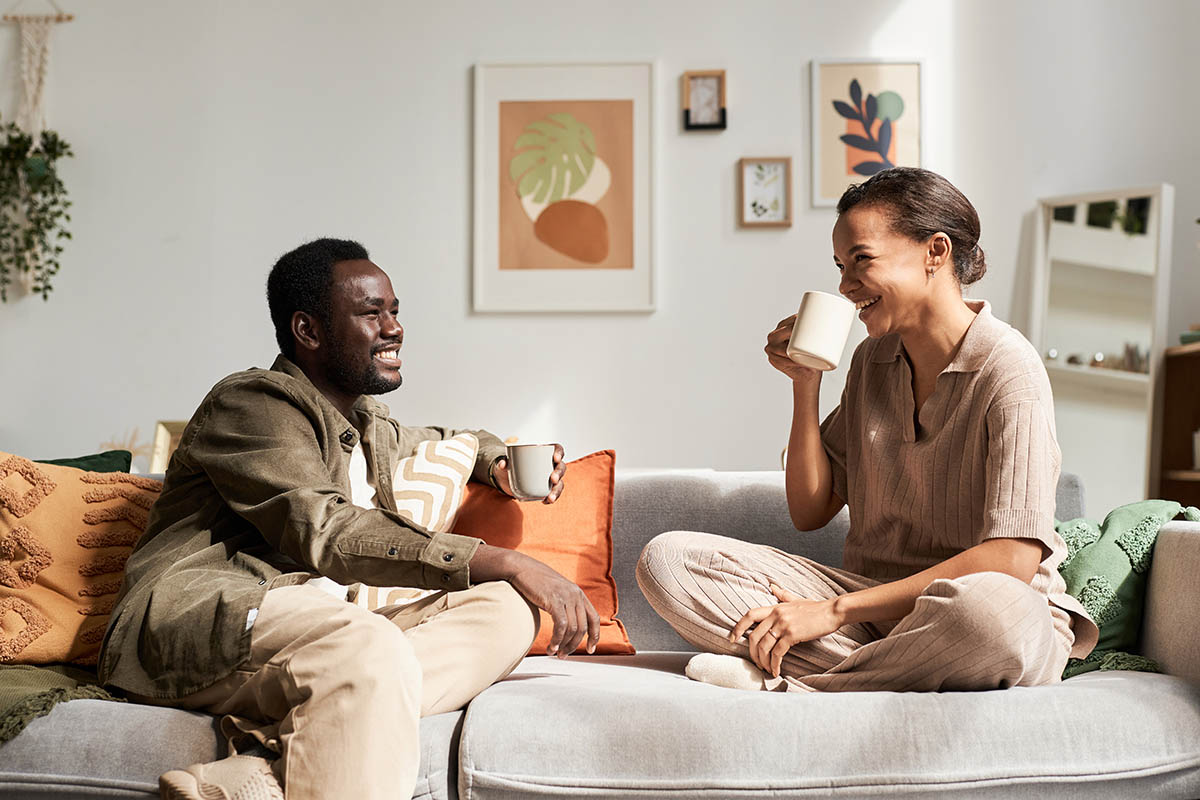 Young Black couple enjoying conversation sitting on couch in cozy home